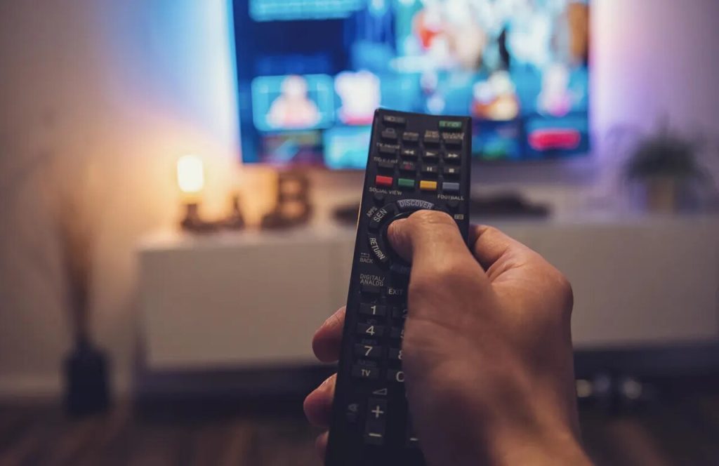 pessoa segurando controle remoto apontando para tv com streaming representando para onde apontar antena digital