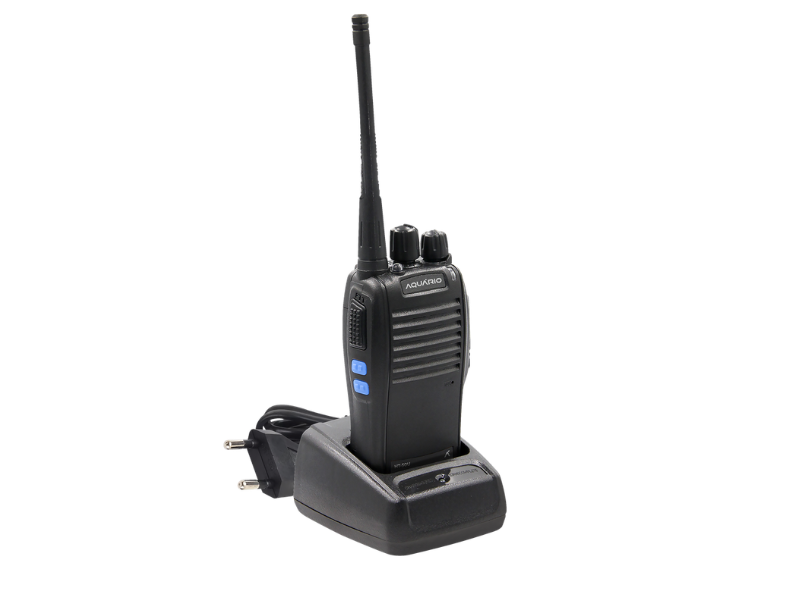 Rádio comunicador portátil Aquário posicionado em sua base carregadora, com antena longa e cabo de alimentação, sobre fundo branco