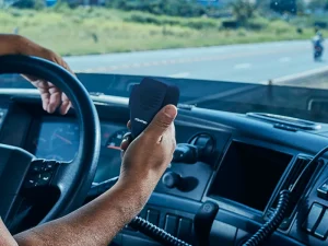 Motorista segurando o microfone PTT de um rádio PX no painel de um caminhão enquanto dirige em uma estrada.